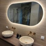 Ovale spiegel op muur met reliëf en geplaatst boven een badkamermeubel met 2 kommen