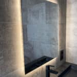 Spiegel op grijze tegelmuur met zwarte kraan